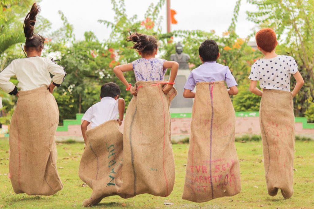 Multiple kids jumping in potato sacks for a race outside.